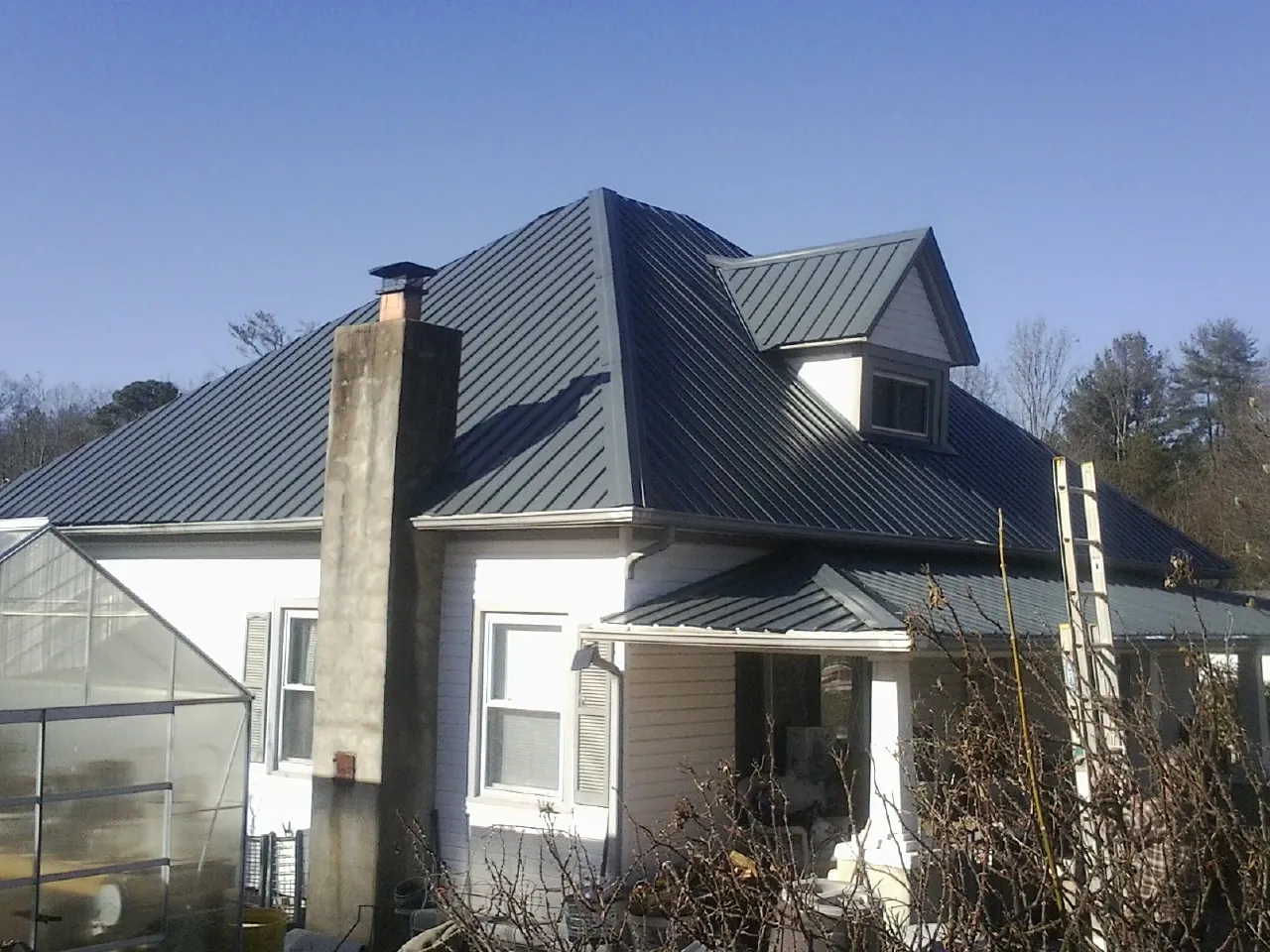 Dark blue standing seam metal roof on a white farmhouse with dormer — Slate & Tile Roof Repair by Roofing Brothers in Eola