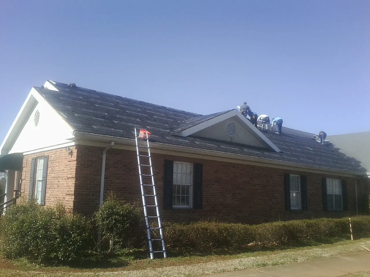 Crew tearing shingles off a brick ranch roof with a ladder set — Emergency Roof Repair work by our crew in Eola