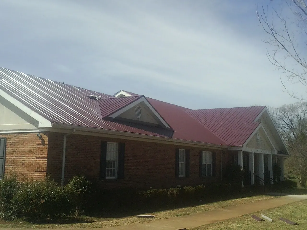 Red metal roof with gabled entries on a long brick building, from a Hail Damage Roof Repair job in Eola