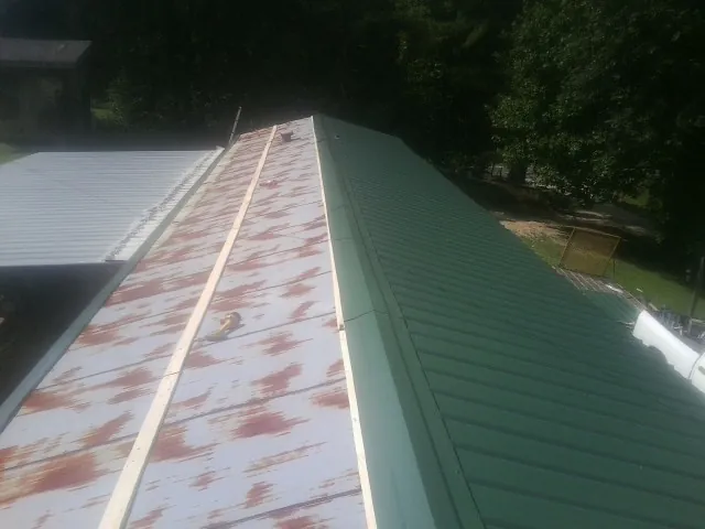 Old rusted panels beside newly installed green metal roofing — Wind Damage Roof Repair by Roofing Brothers in Eola