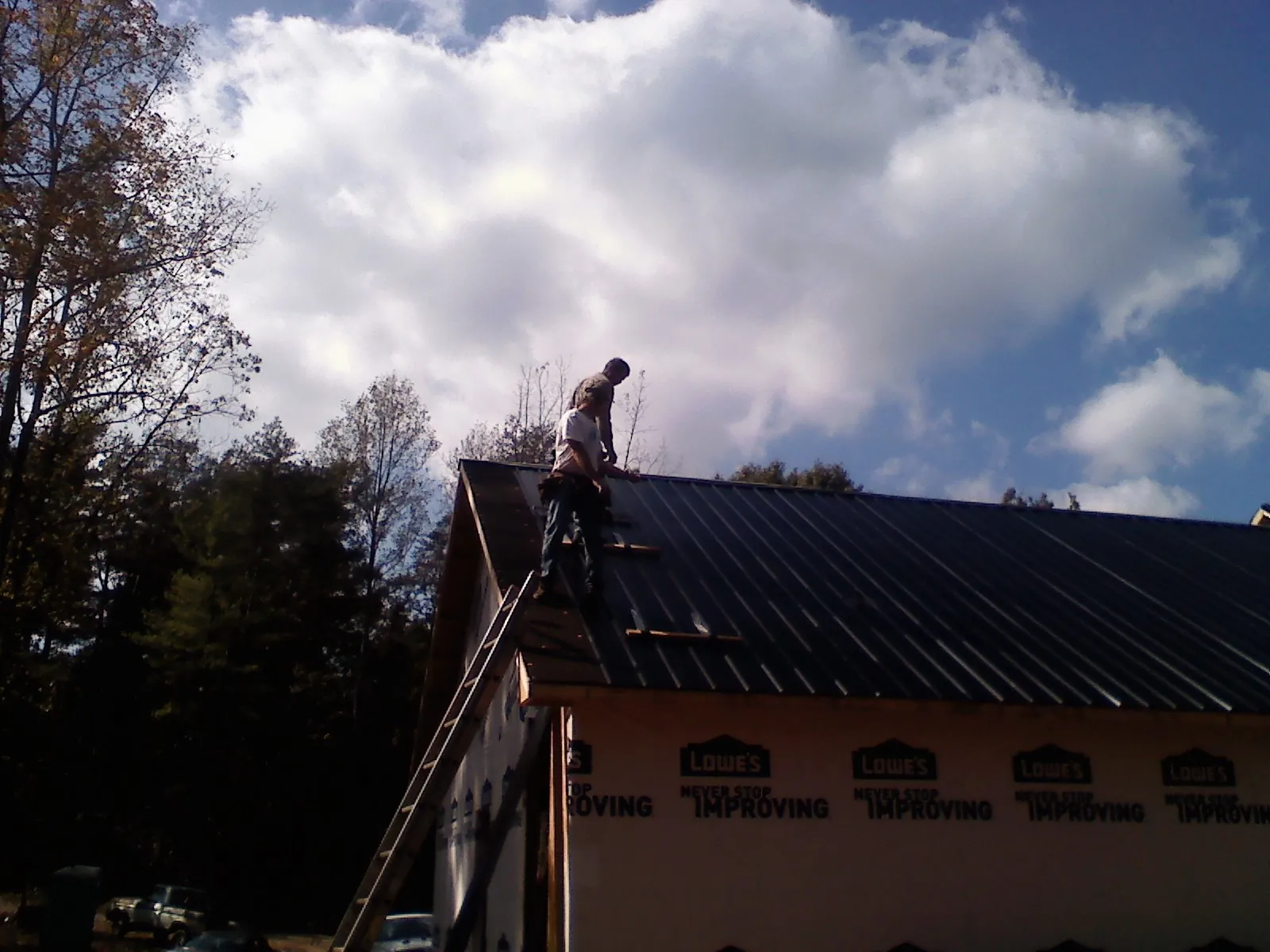 Roofer fastening dark metal panels high against a cloudy sky, from a Roof Inspection job in Eola